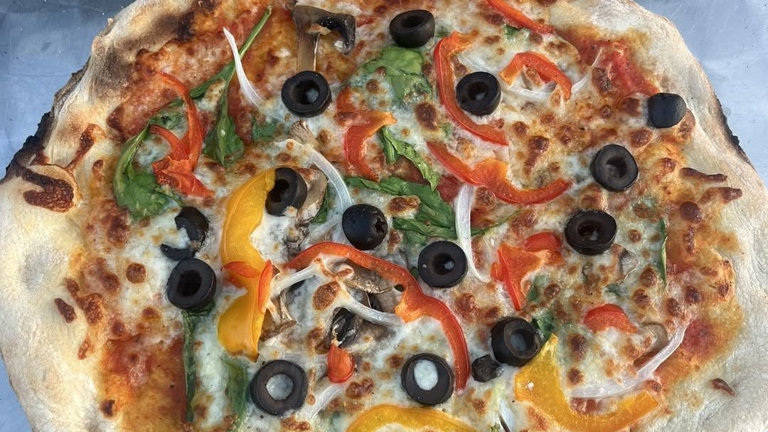 A loaded veggie wood-fired pizza with peppers, olives, mushrooms and spinach